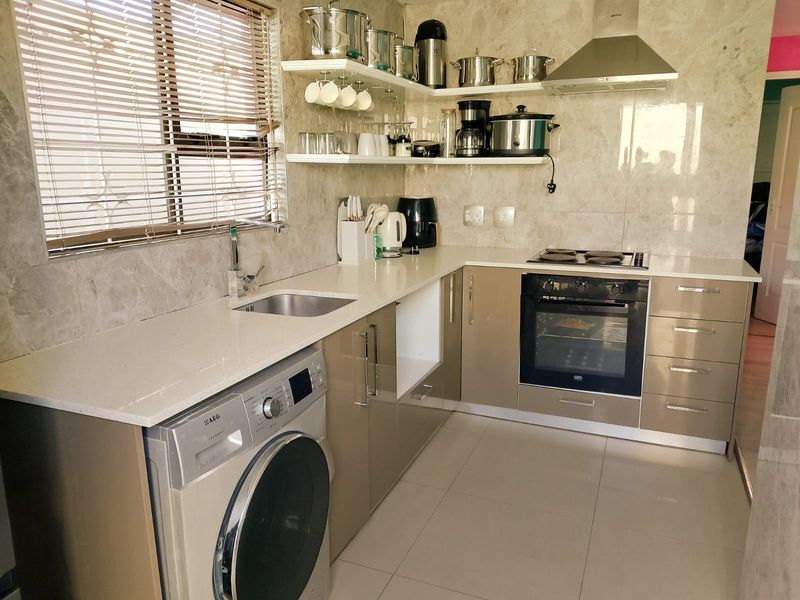 Modern kitchen featuring stone countertops, built-in oven, electric hob, stainless steel extractor fan, and ample cabinetry with integrated laundry appliance space.