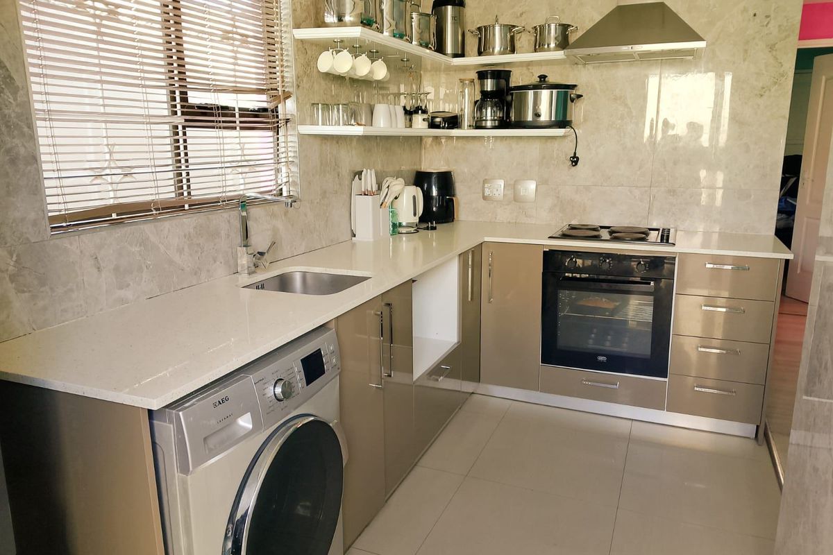 Modern kitchen featuring stone countertops, built-in oven, electric hob, stainless steel extractor fan, and ample cabinetry with integrated laundry appliance space.