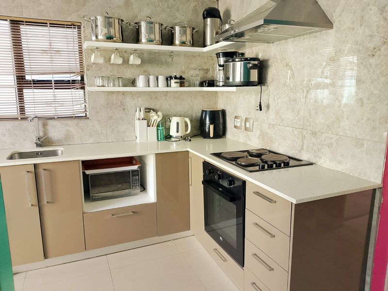 Modern kitchen featuring sleek cabinetry, stone countertops, built-in oven, electric hob, extractor fan, and stylish tiled splashback with convenient floating shelving.