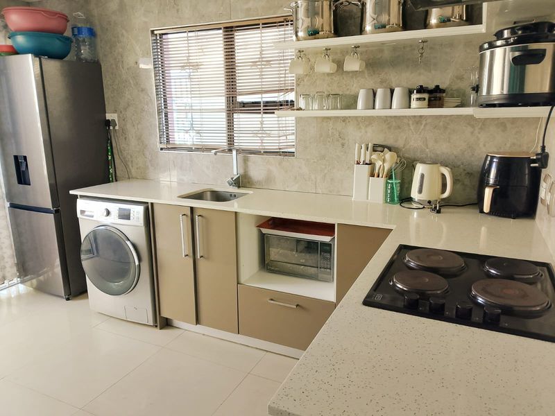 Modern kitchen featuring stone countertops, integrated washing machine, electric hob, and stylish floating shelving with neutral cabinetry and tiled splashback.