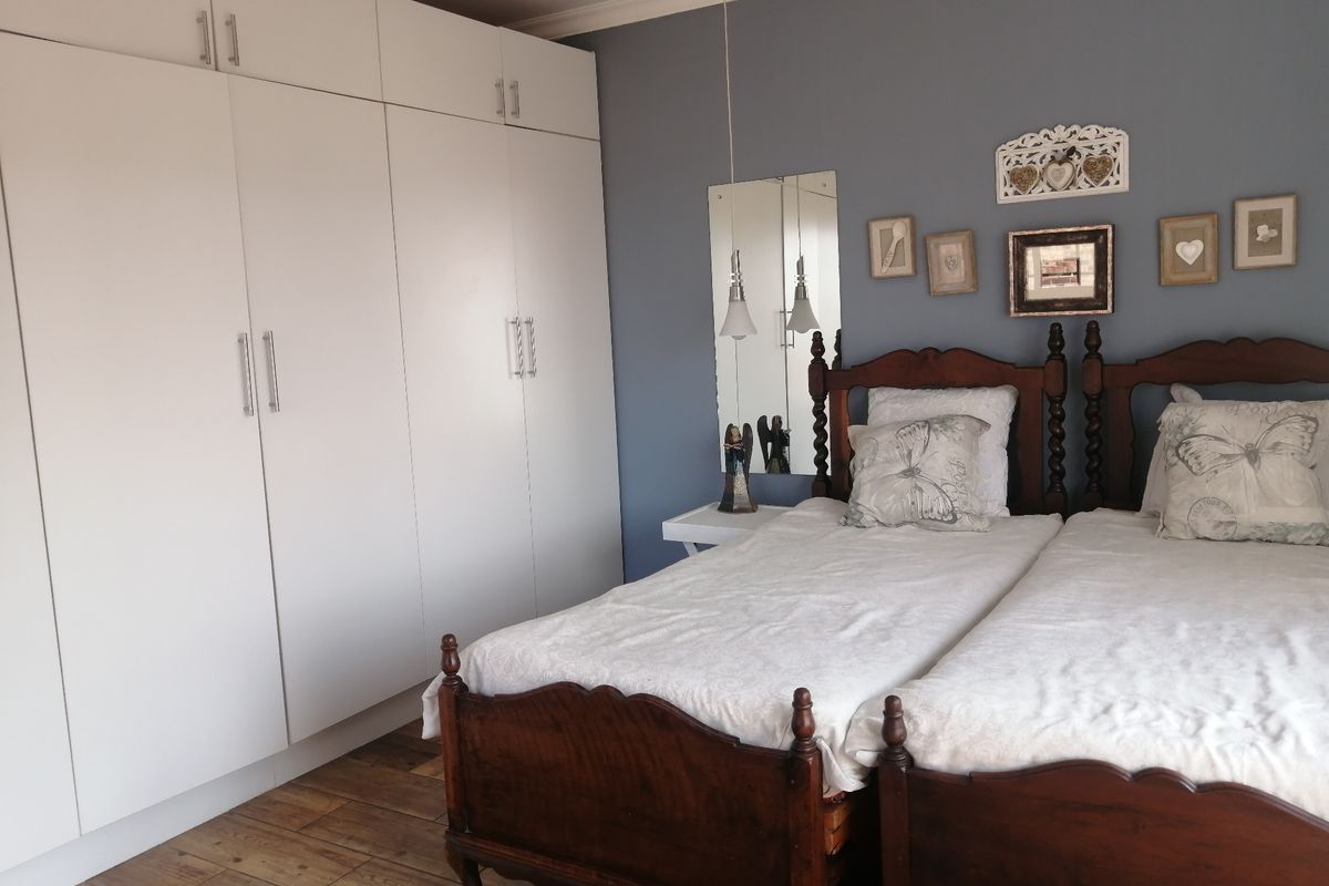 A well-maintained bedroom featuring timber flooring and extensive floor-to-ceiling built-in cupboards with a neutral blue accent wall.