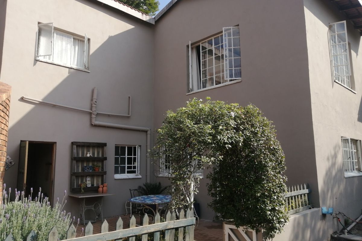 Rear exterior view of the house featuring a paved patio area, casement windows, and a timber picket fence.
