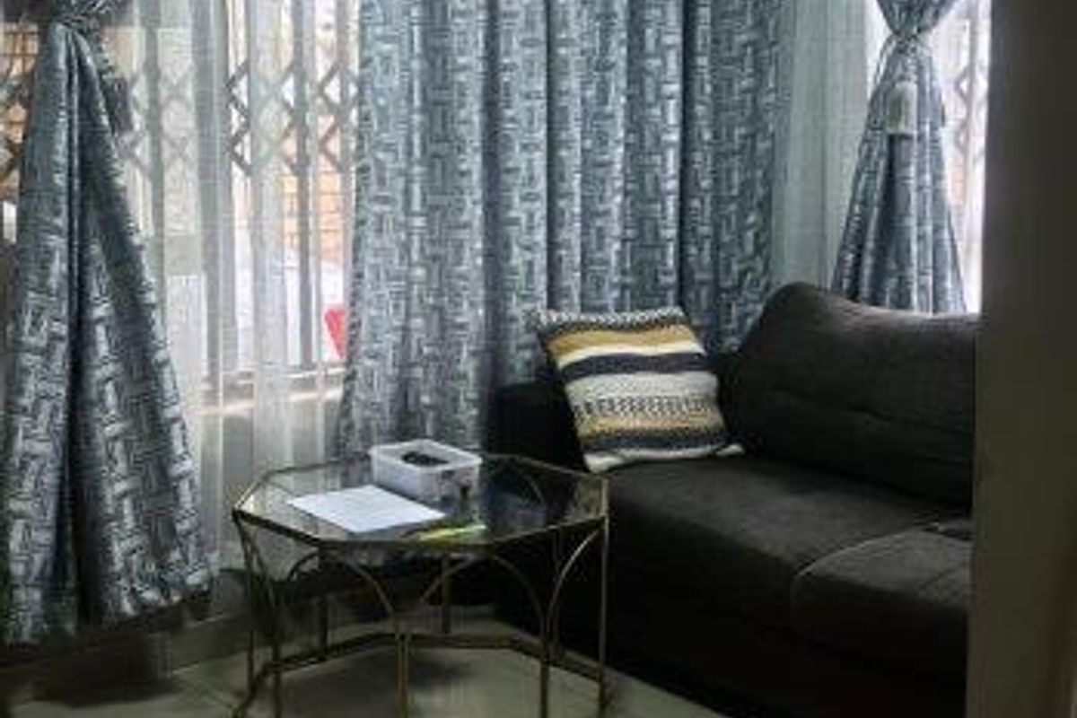 A living room area featuring large format floor tiles, a central ceiling light, and windows fitted with security gates.