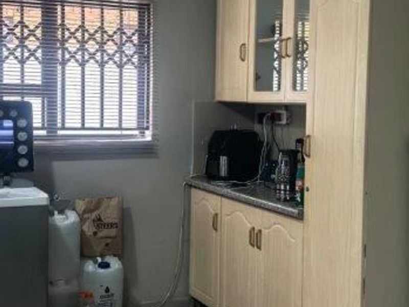 A functional kitchen area featuring light-toned laminate cabinetry, tiled flooring, and a window fitted with a security gate.