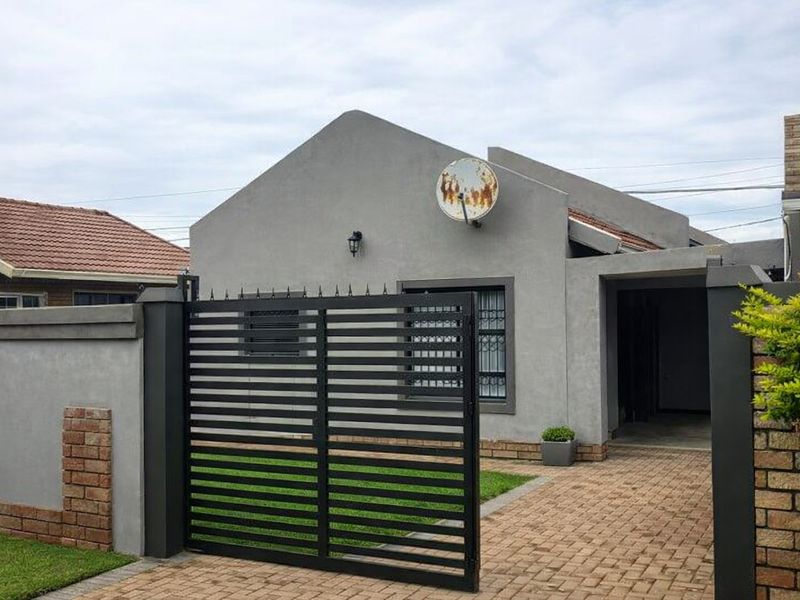 Front view of a modern house featuring a paved driveway, secure metal gate, and perimeter walling.