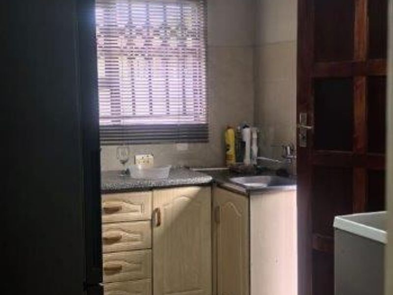 A compact kitchen featuring built-in cabinetry, tiled flooring, and a stainless steel sink, offering a functional space with potential for cosmetic updates.