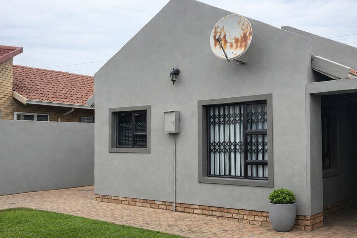 Rear exterior view of the property featuring a paved walkway, security gates on windows, and a rendered facade.