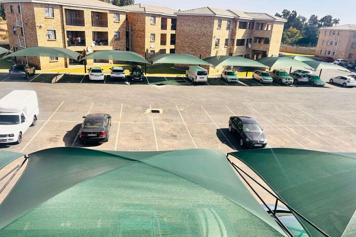 Elevated view of the townhouse complex parking area featuring multiple shade cloth carports and brick building facades.