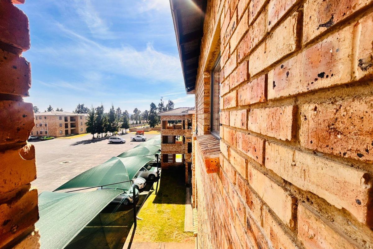 An elevated view of the townhouse complex exterior, featuring face brick walls, paved parking areas with shade cloth carports, and surrounding communal grounds.