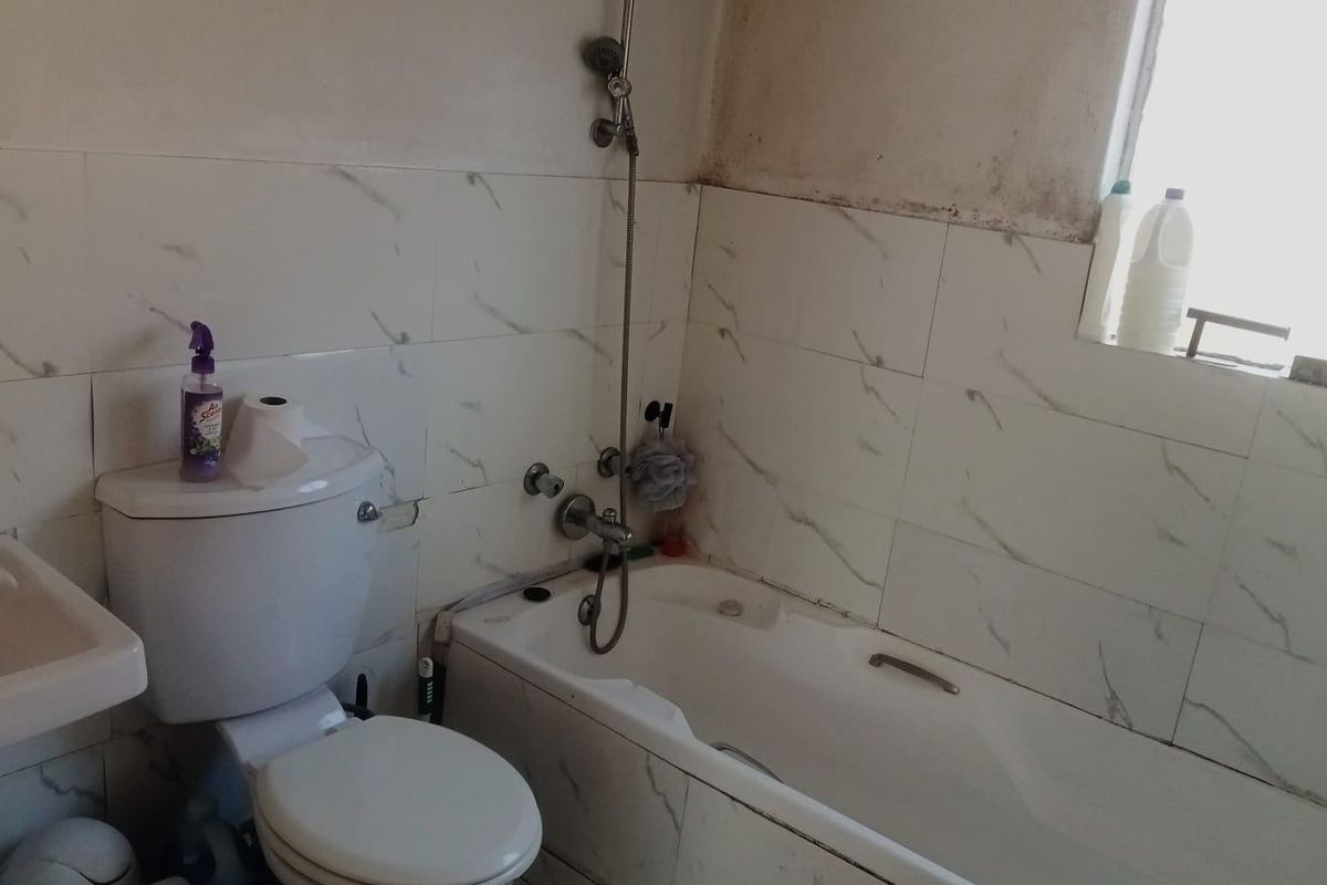 A functional bathroom featuring a bathtub with shower mixer, pedestal basin, and toilet, finished with marble-effect wall tiles.