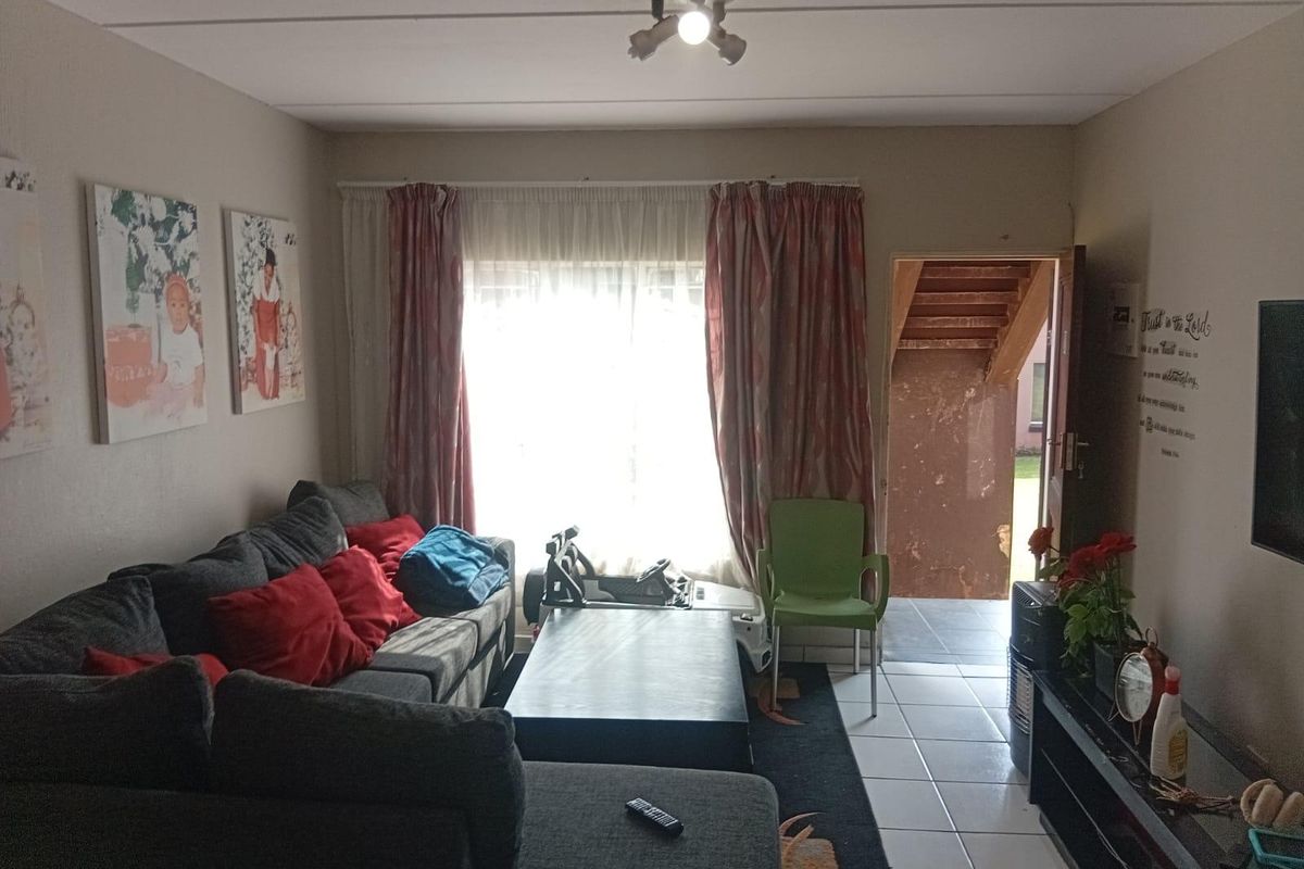 A living room area featuring tiled flooring and direct access to an exterior entrance, with neutral wall finishes and a central ceiling light fixture.