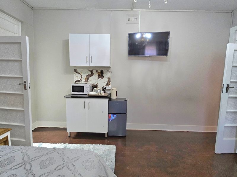 A bedroom featuring a compact kitchenette area with built-in cabinetry, stone-look splashback, and a wall-mounted television.
