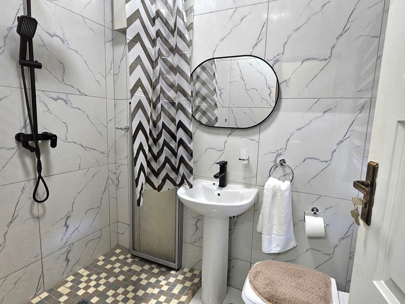 A modern bathroom featuring marble-effect wall tiles, a pedestal sink with a black mixer tap, and a shower area.