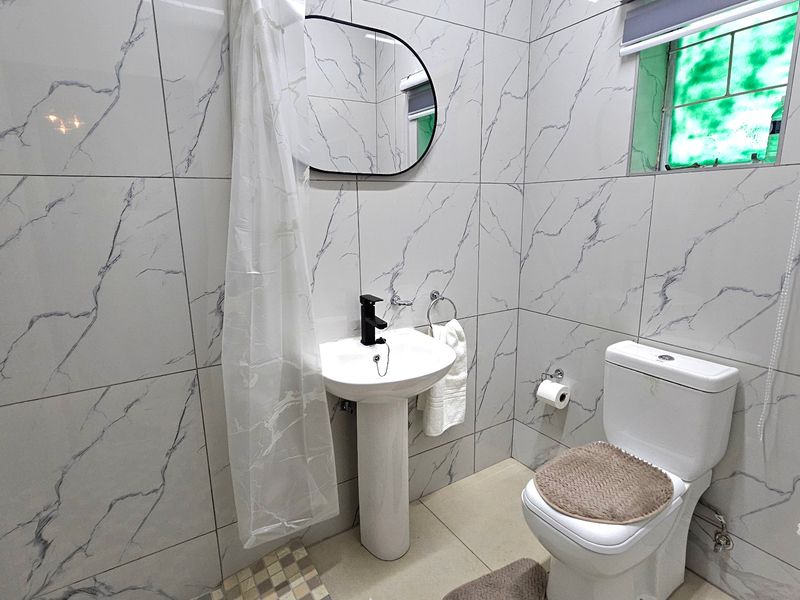 A modern bathroom featuring marble-look wall tiles, a pedestal basin with a black mixer tap, and a standard toilet.
