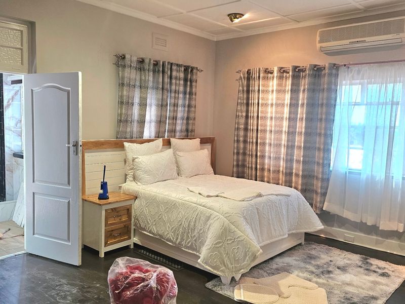 Spacious bedroom featuring an en-suite bathroom, air conditioning unit, and neutral finishes, offering a comfortable and functional living space.