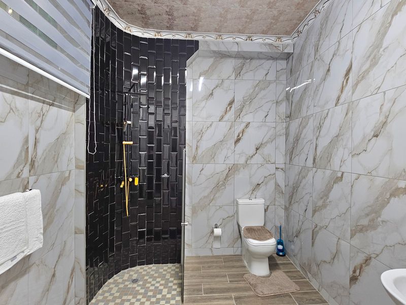 Modern bathroom featuring a walk-in shower with black subway tiles, marble-effect wall tiling, a toilet, and a vanity basin with a round mirror.