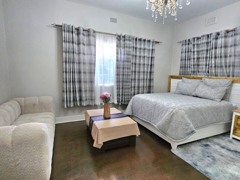 Spacious bedroom featuring polished concrete flooring, a decorative crystal chandelier, and a custom built-in headboard with integrated bedside storage.