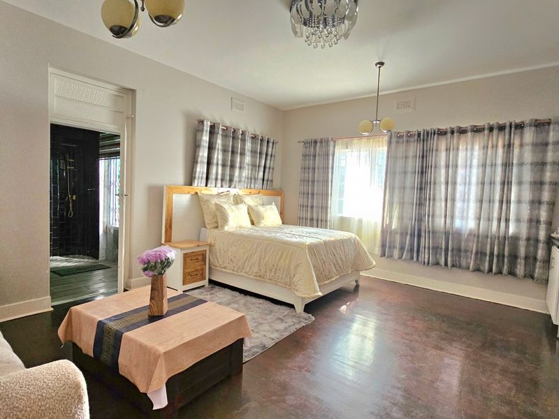Spacious bedroom featuring polished hardwood flooring, neutral wall finishes, and direct access to an adjoining bathroom.