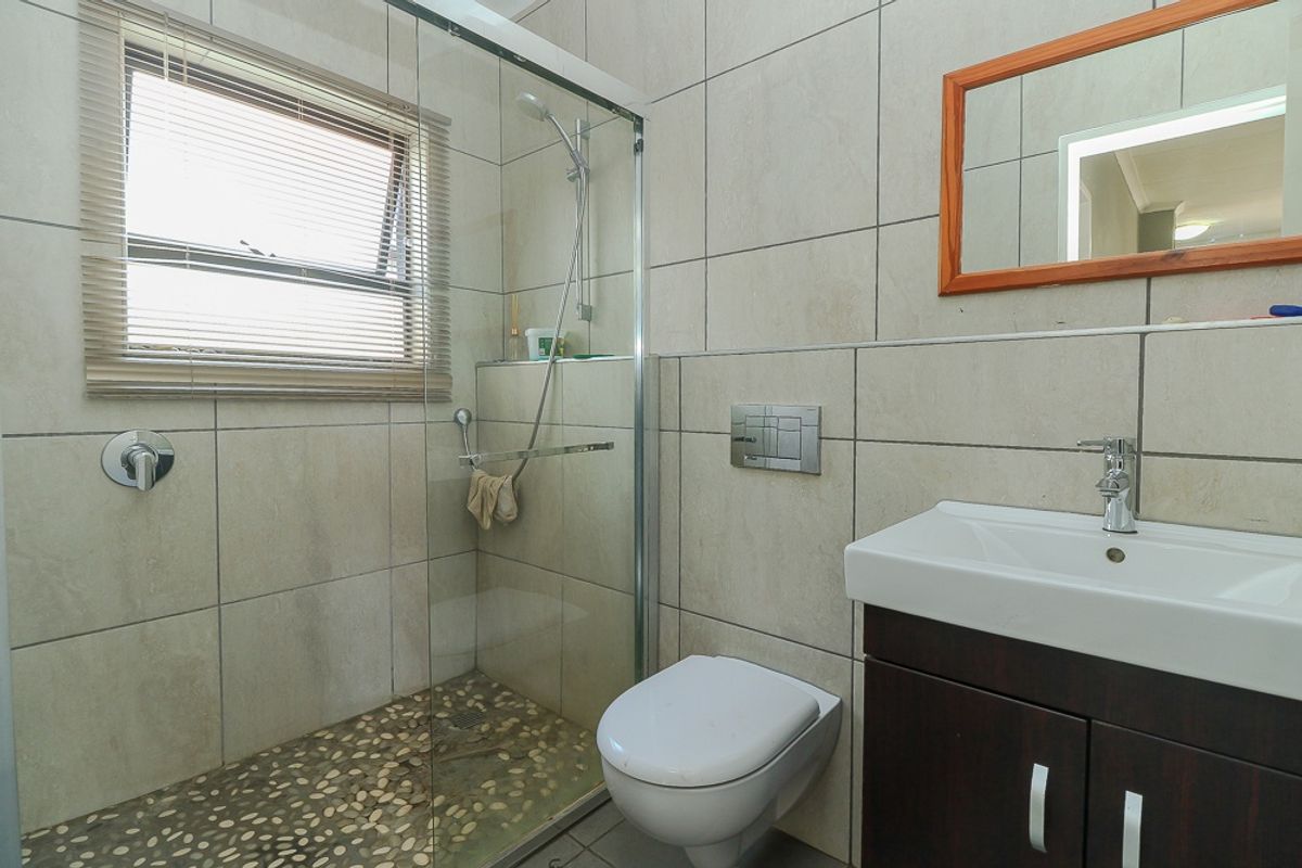 Modern bathroom featuring a walk-in shower with pebble flooring, wall-mounted toilet, and a vanity cabinet with basin.