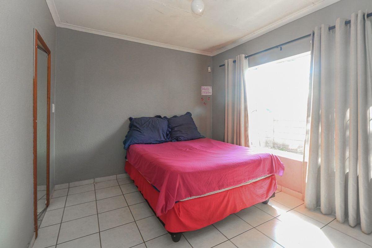 A bedroom featuring tiled flooring, neutral grey walls, and a window with curtain fixtures.