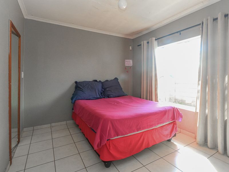 A bedroom featuring tiled flooring, neutral grey walls, and a window with curtain fixtures.
