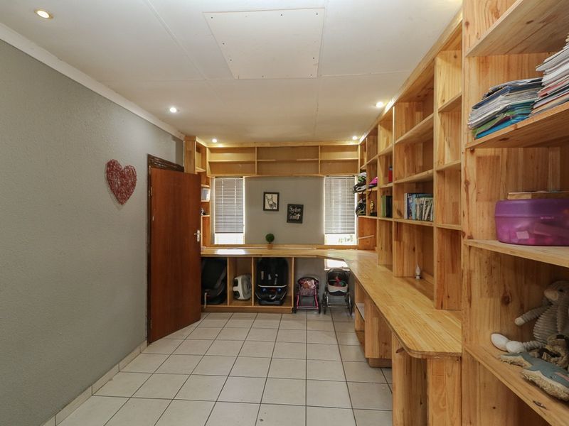 A functional utility room or study area featuring extensive built-in wooden shelving, a wrap-around desk, tiled flooring, and recessed ceiling lighting.