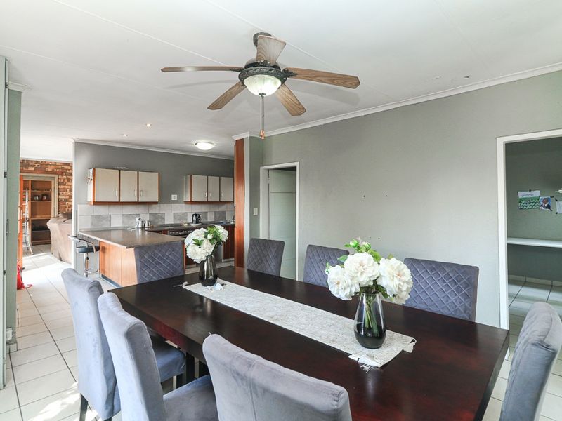 Open plan dining area flowing into a functional kitchen with tiled flooring, neutral wall finishes, and a central ceiling fan.