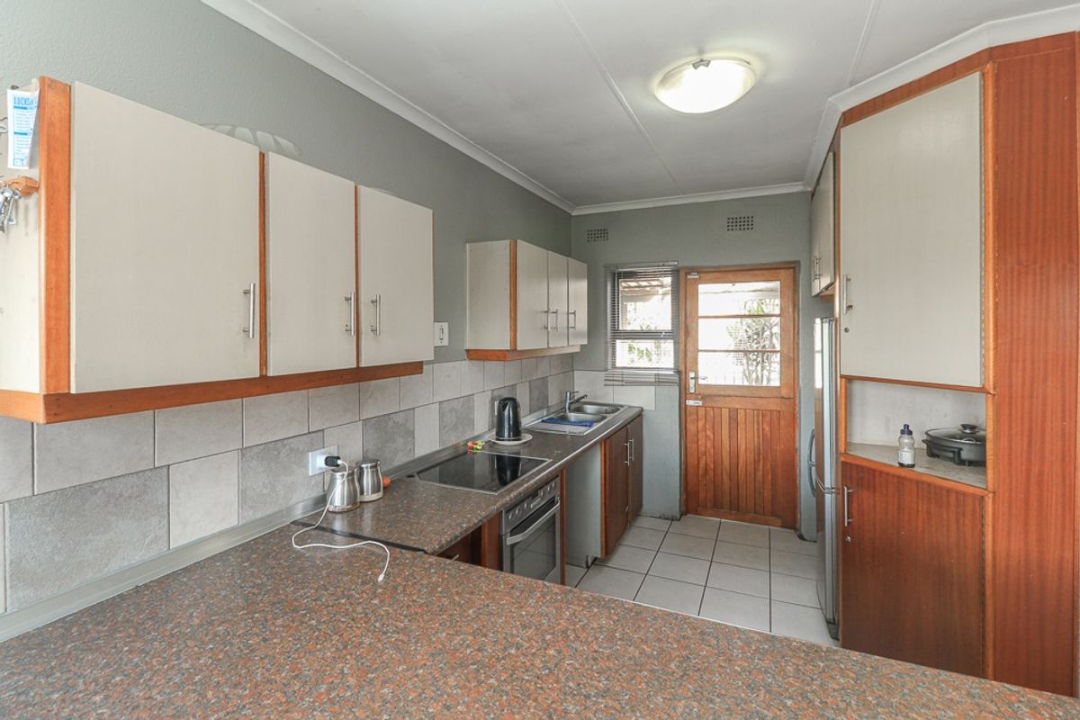 A functional kitchen featuring laminate countertops, built-in cabinetry, a ceramic tile backsplash, and direct access to the exterior via a timber door.