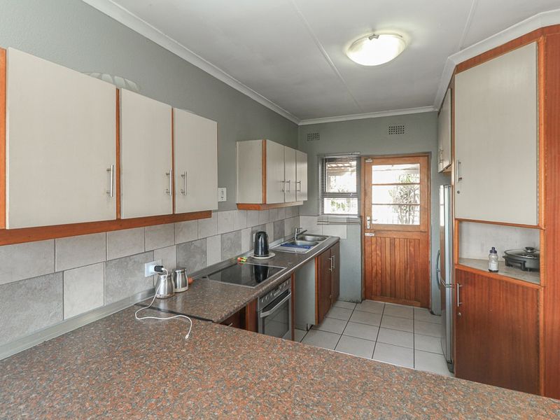 A functional kitchen featuring laminate countertops, built-in cabinetry, a ceramic tile backsplash, and direct access to the exterior via a timber door.