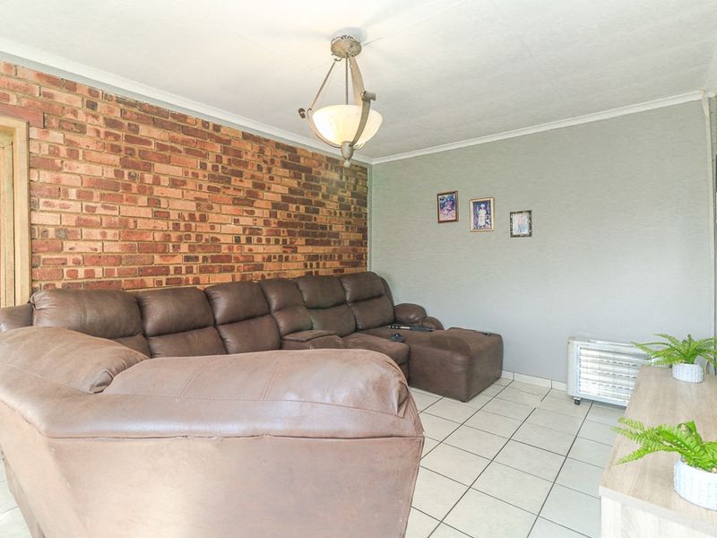 A living room featuring an exposed brick accent wall, neutral painted walls, and ceramic floor tiling.