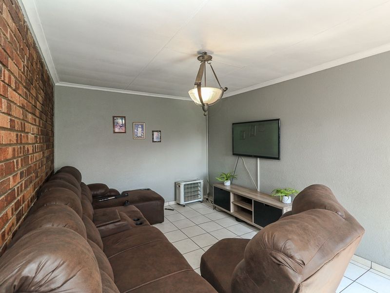 A living room featuring an exposed brick feature wall, neutral painted walls, and ceramic floor tiles, providing a functional and comfortable living space.