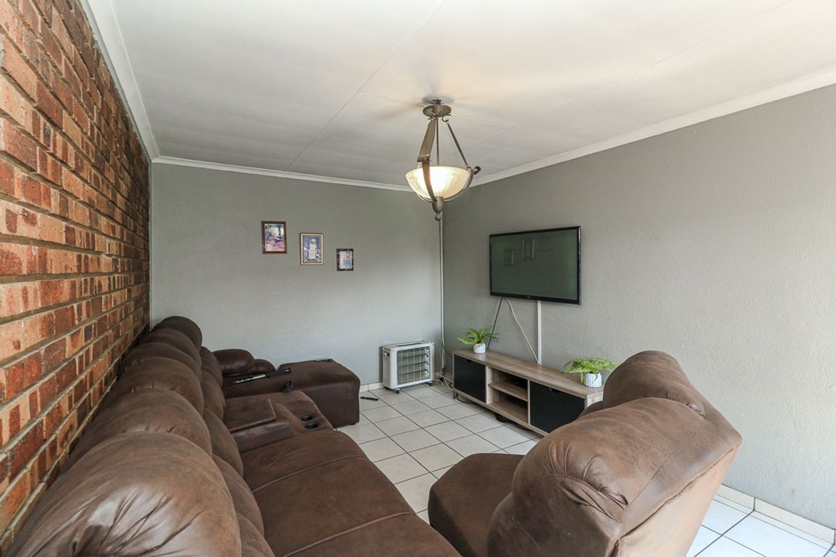 A living room featuring an exposed brick feature wall, neutral painted walls, and ceramic floor tiles, providing a functional and comfortable living space.