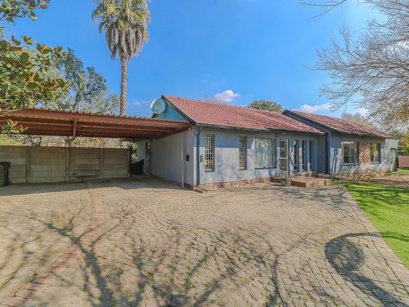 Front exterior view of a single-story house featuring a paved driveway, attached carport, and established garden surroundings.