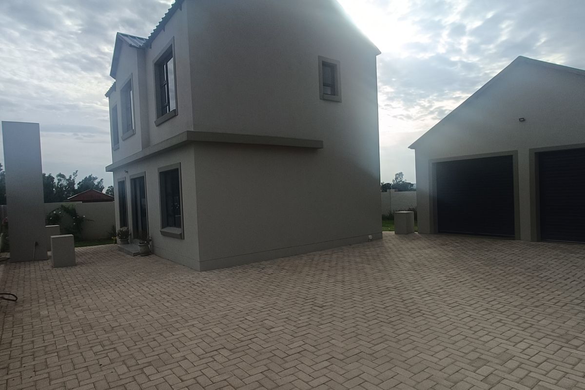 A view of the rear exterior featuring a two-story house, a double garage, and an extensive paved driveway area.