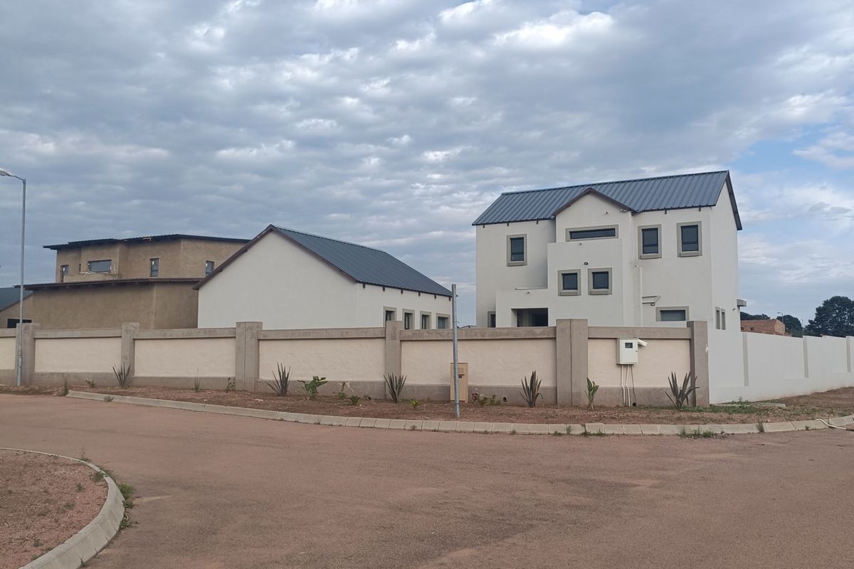 A view of a modern residential property featuring a perimeter wall, metal roofing, and paved street access in a suburban setting.