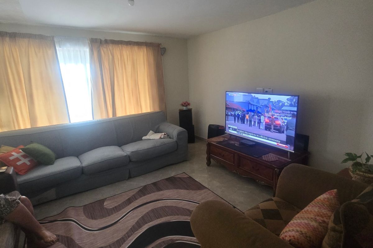 A living room featuring tiled flooring and large windows with curtains. The space requires cosmetic updates to the ceiling and lighting fixtures.