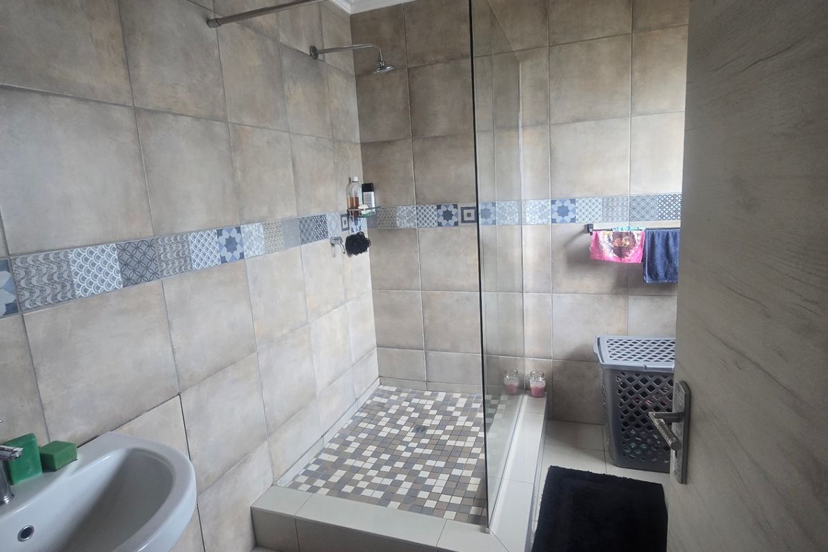 A functional bathroom featuring a walk-in shower with a glass screen, pedestal basin, and neutral wall tiling. The ceiling requires finishing.