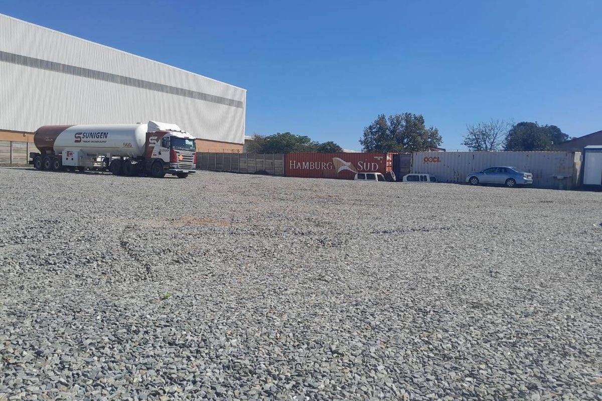 Large industrial gravel yard featuring a warehouse building and perimeter fencing, suitable for logistics or storage operations.