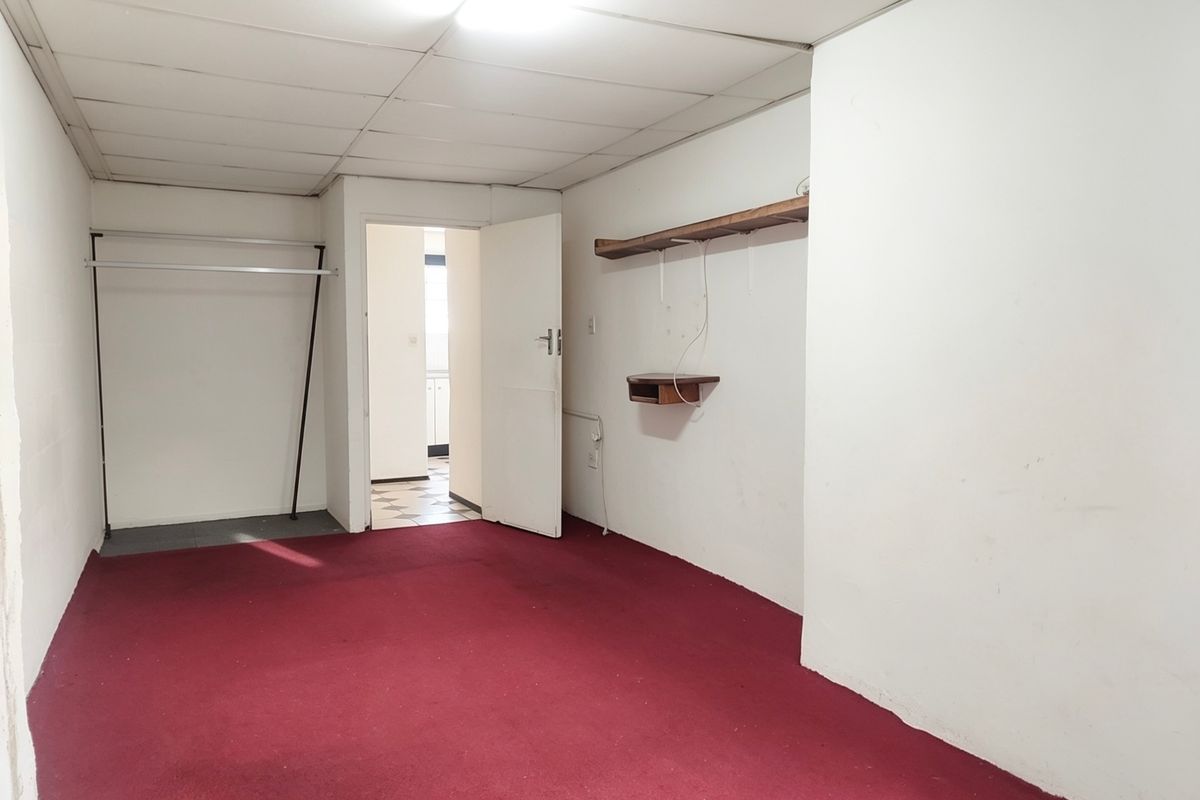 An empty bedroom featuring a drop ceiling, built-in shelving, and a hanging rail, requiring cosmetic updates to the flooring and wall finishes.