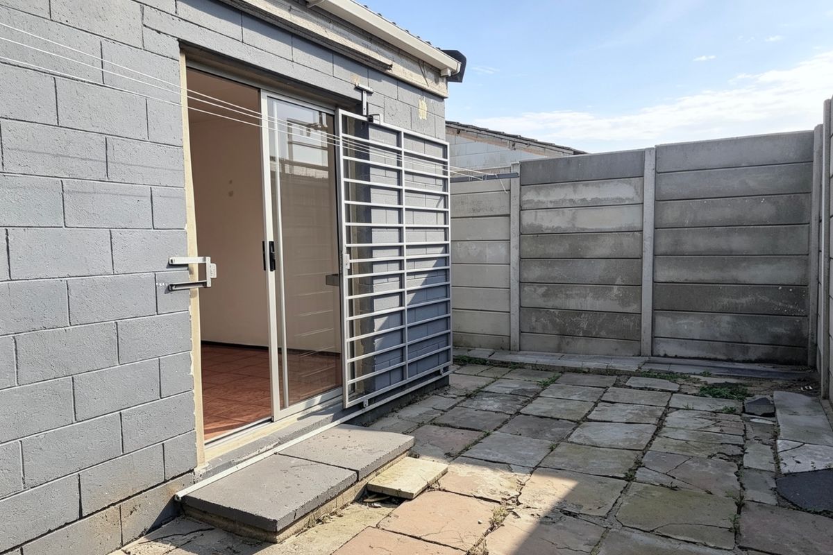 Rear exterior view featuring a paved patio area, concrete block wall construction, and a sliding glass door with a security gate.