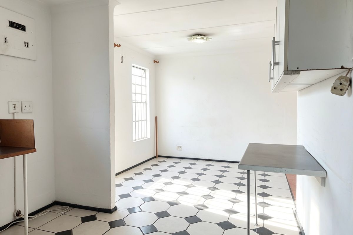 An empty kitchen area featuring distinctive geometric floor tiles, wall-mounted cabinetry, and a window with security bars, offering a blank canvas for renovation.