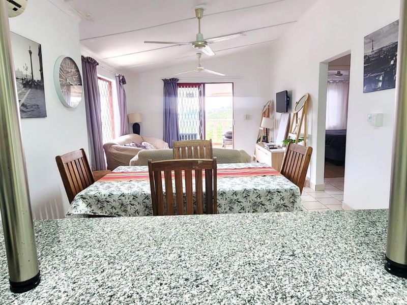 Open-plan living and dining area featuring tiled flooring, ceiling fans, and a granite breakfast bar, with direct access to an outdoor patio.