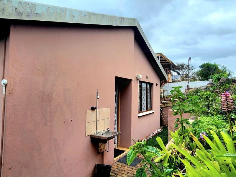 Rear exterior view of the townhouse featuring a paved walkway, garden area, and a functional wall-mounted utility sink.