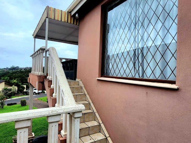 Exterior view of the rear facade featuring an external staircase, balustrade, and a covered landing area with a window security grille.