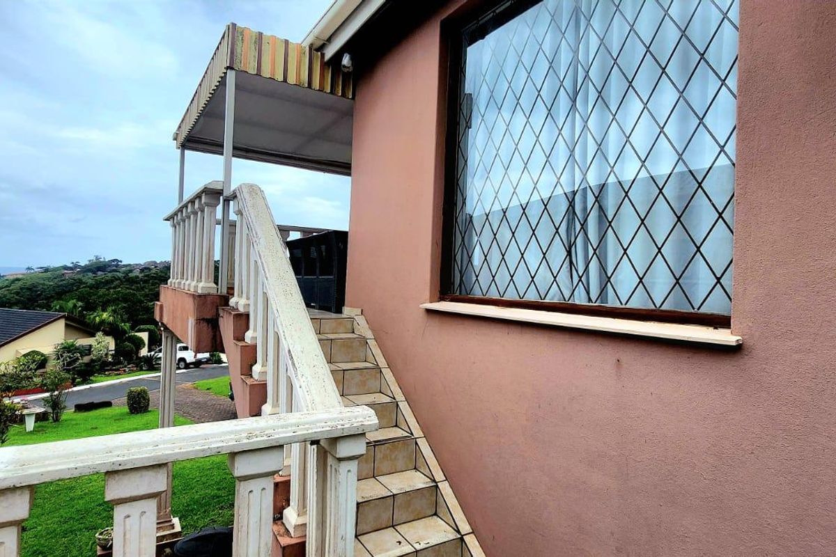 Exterior view of the rear facade featuring an external staircase, balustrade, and a covered landing area with a window security grille.
