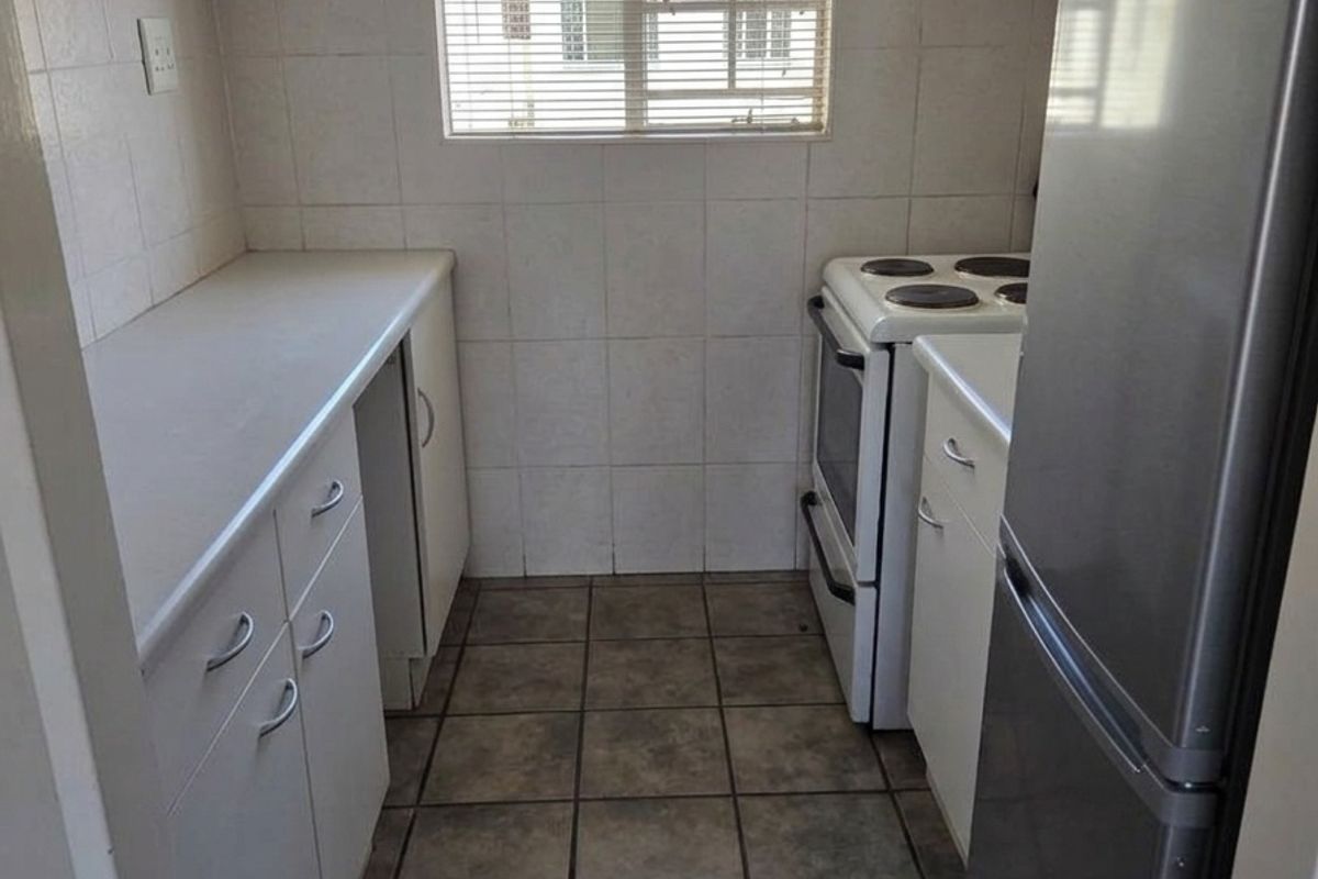 A compact kitchen featuring tiled flooring, white cabinetry with laminate countertops, and a freestanding stove, requiring cosmetic updates to the cabinetry.