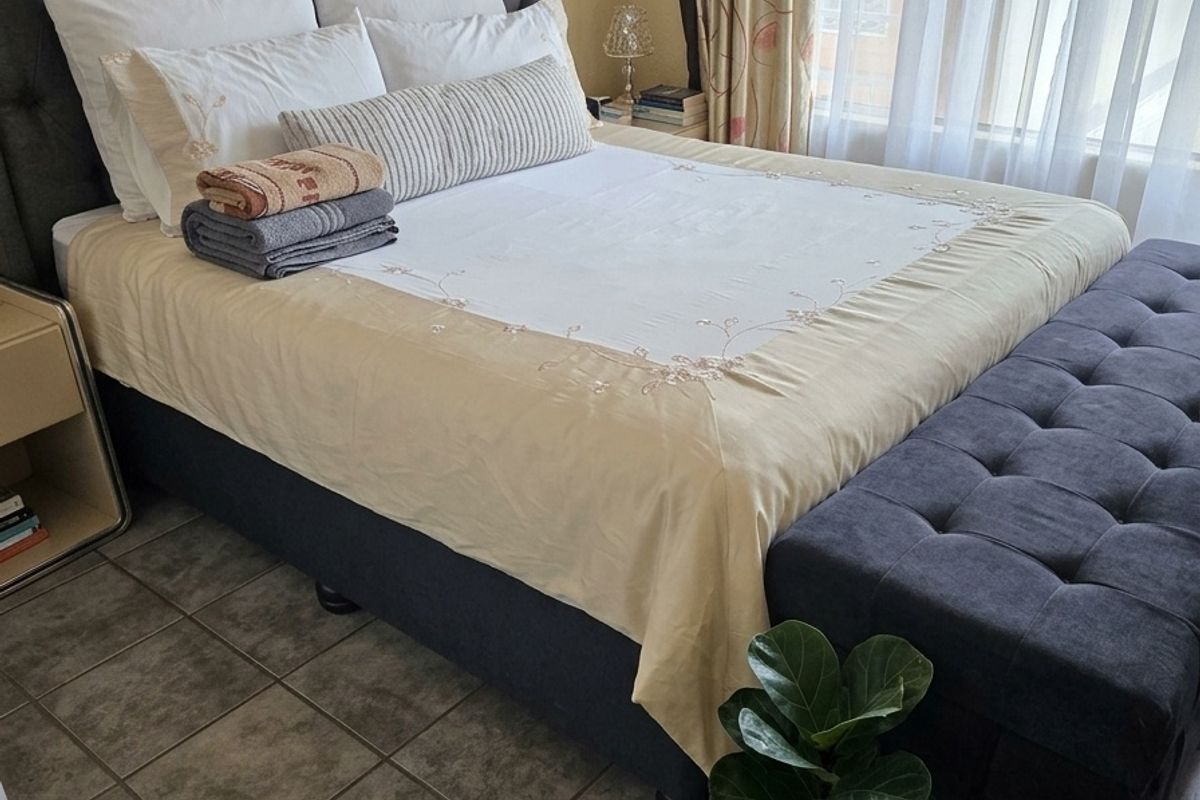 A bedroom featuring tiled flooring and large windows with curtains, providing a functional and comfortable sleeping space.