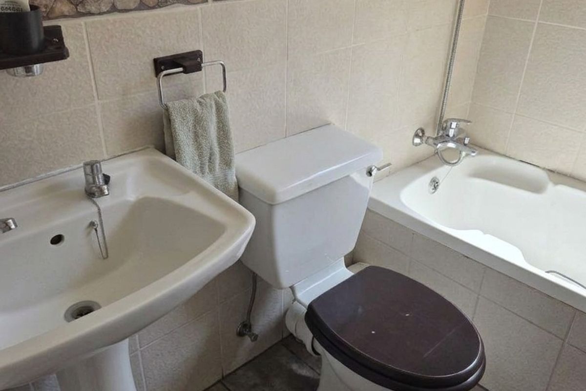 A functional bathroom featuring a pedestal washbasin, toilet, and bathtub with tiled walls and a decorative stone-effect border.