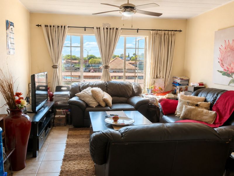 A comfortable living room featuring tiled flooring, a ceiling fan, and large windows that provide natural light and views of the surrounding area.