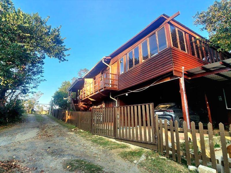 Exterior view of a timber-clad townhouse featuring a raised balcony, integrated carport, and timber fencing along a gravel driveway.